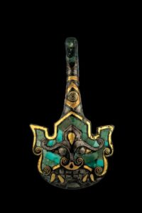 Bronze belt hook with gold, silver and turquoise inlays in the shape of an orc face (De-Neng-Tang Collection). Also a dazzling turquoise-inlaid piece, the orc-shaped hook is decorated with a demigod with rounded eyes, a wide nose and a fanged mouth. It is filled with curved turquoise tiles varying in shape and size but arranged pleasingly. The particularly refined eyebrows of the orc are depicted with a pattern of slanted lines.